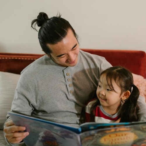 a man and a child sitting on a couch looking at a book